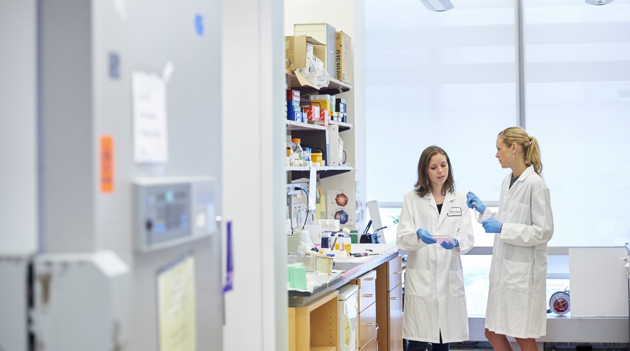 Two female researchers in lab coats discussing findings