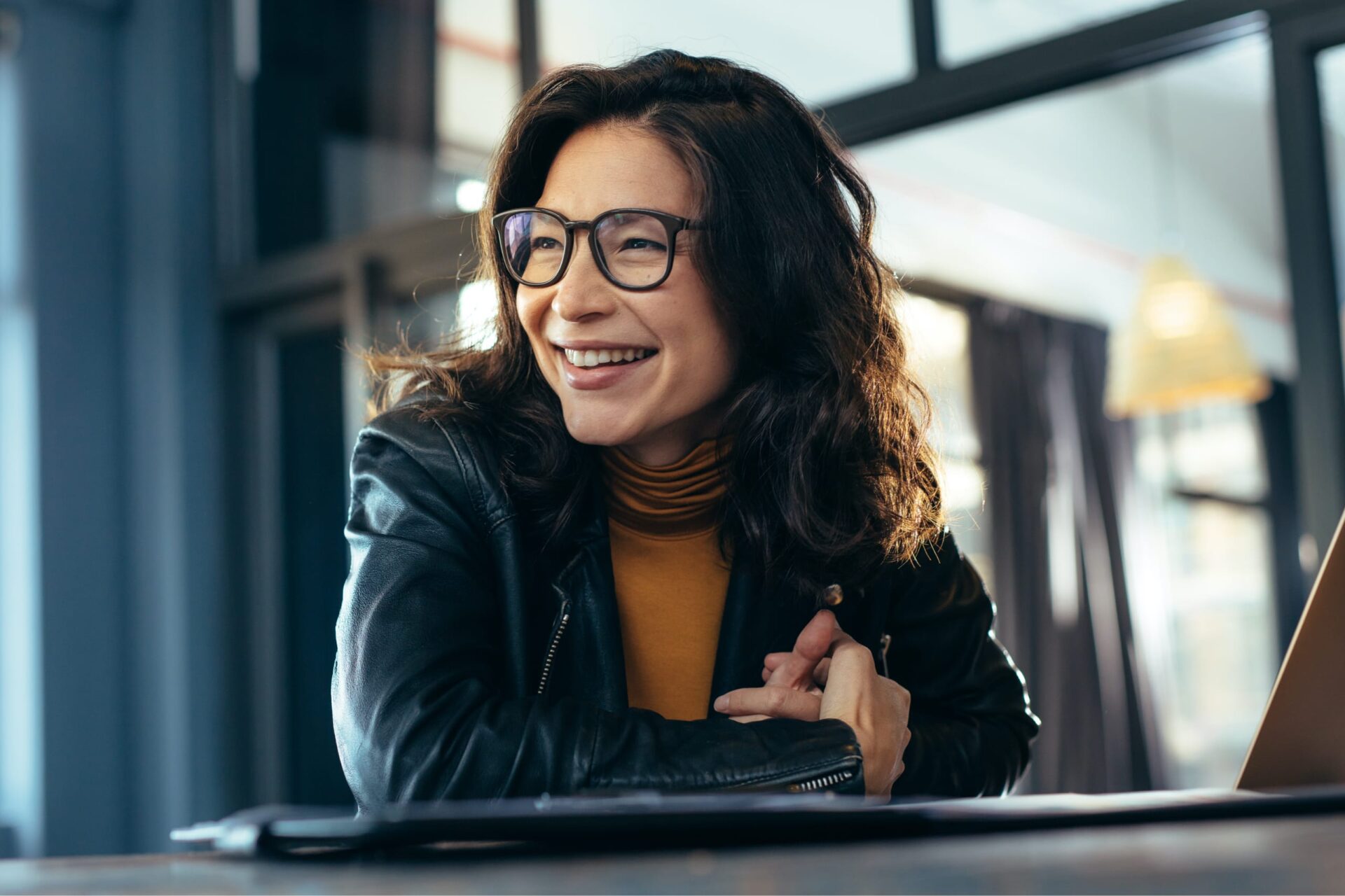 A woman with glasses leaning over a tab and looking to the side while smiling