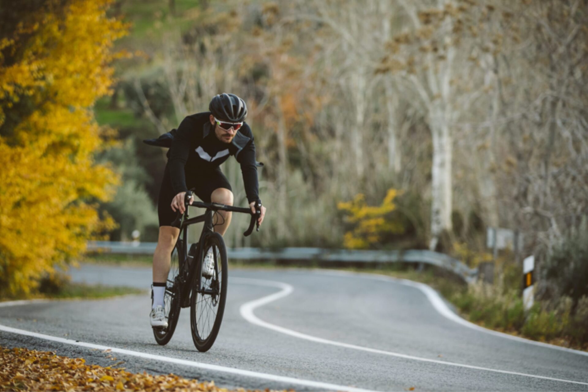 A cyclist wearing a helmet and riding on a curved road in front of fall foliage