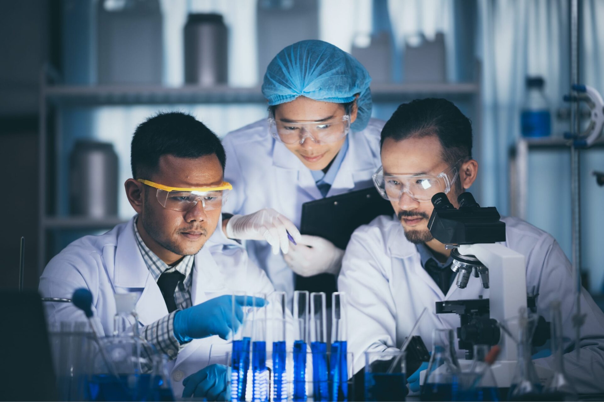 Three researchers gathered in a low-light room looking at a set of tubes