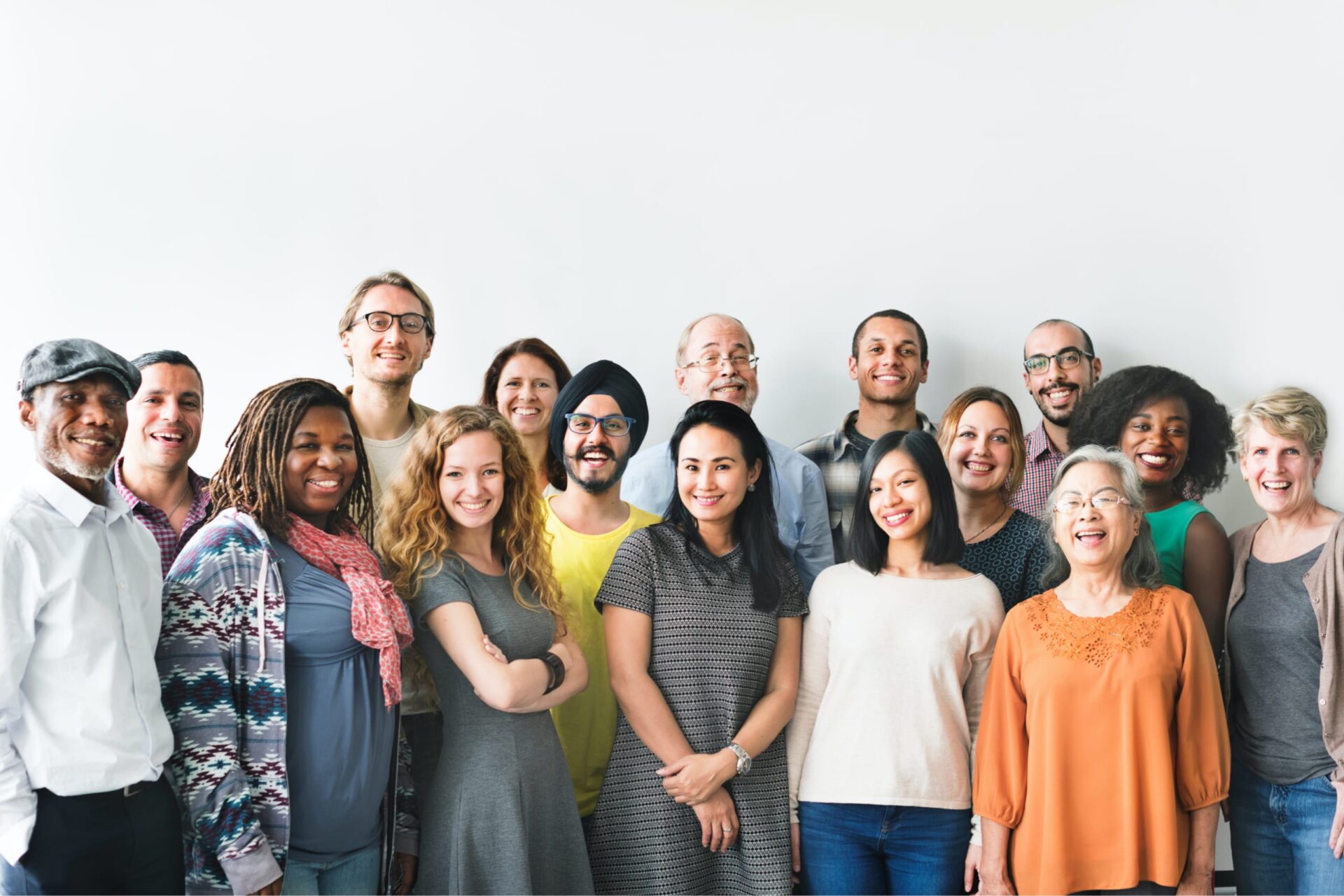 A multiethnic group of people standing against a wall and smiling into the camera