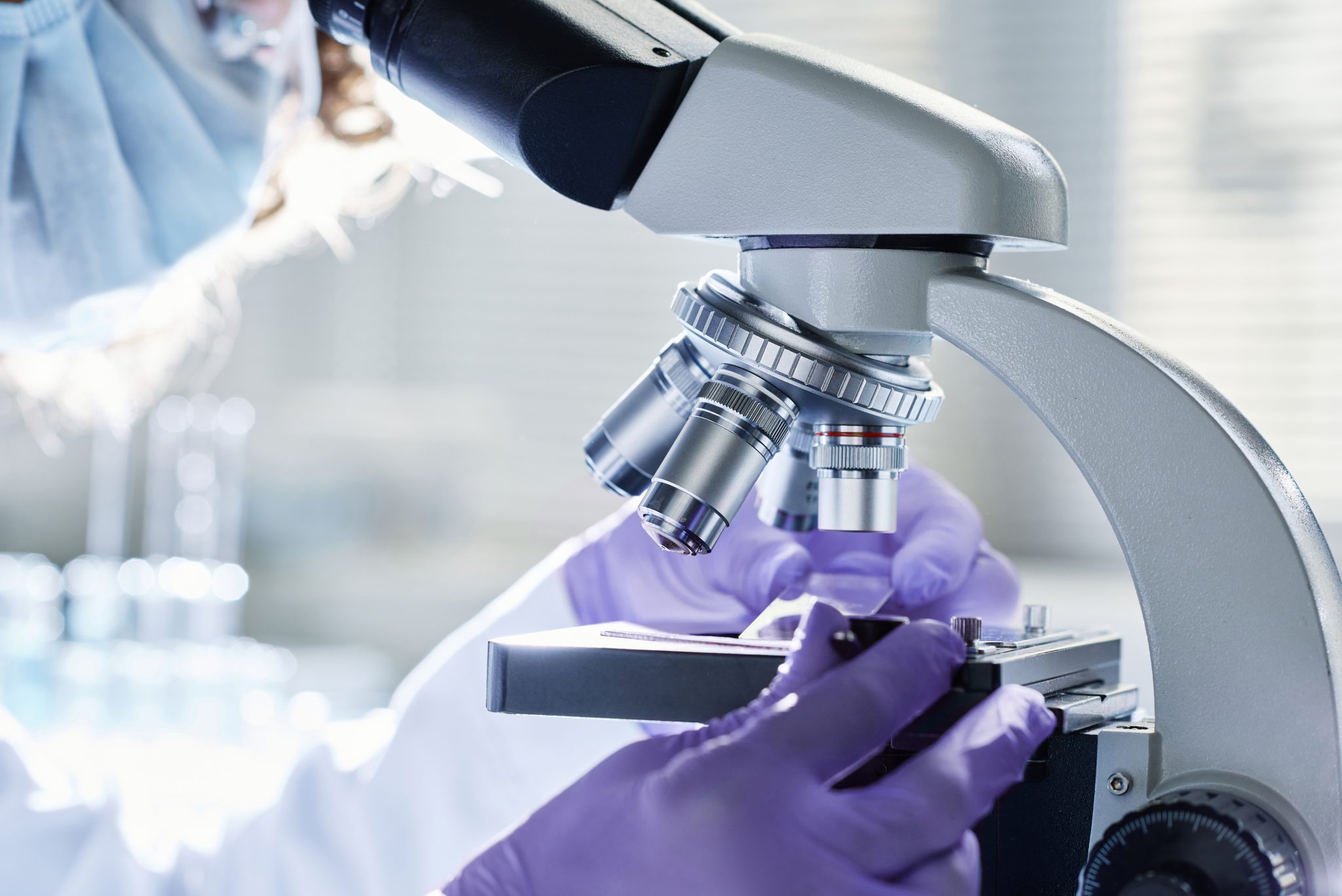 A scientist wearing gloves looking into a microscope