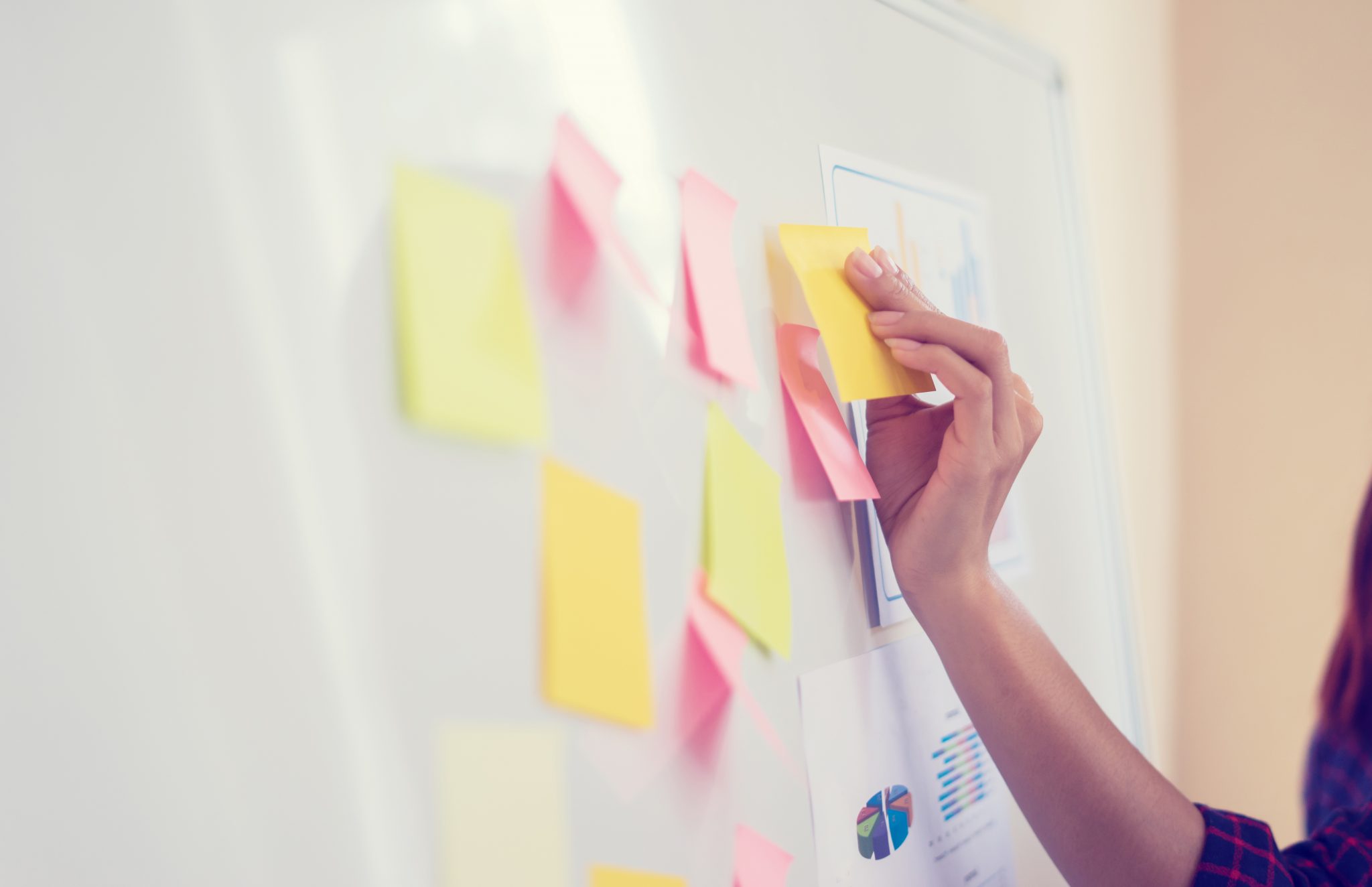 A hand reaching up to place sticky notes on a board